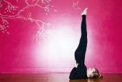 Frau macht in Yogastudio vor rotem Hintergrund Schulterstand yoga-schulterstand